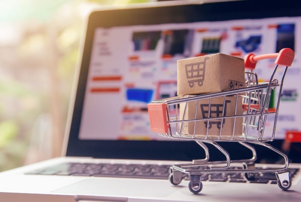 Gambar dari laptop yang menampilkan layanan jualan online vs offline yang direpresentasikan troli belanja di atas laptop